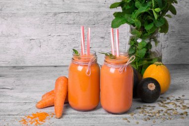 Parlak turuncu smoothies büyük mason kavanoz havuç, kabaklari ve gri arka plan., yeşil bitki ile yakın çekim. Detoks kavramı.