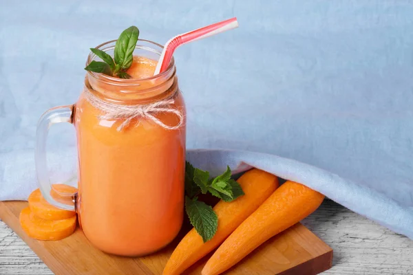 Крупный план красивого коктейля из морковного смузи на синем фоне. Детоксикационный напиток в банке каменщика рядом с морковью . — стоковое фото