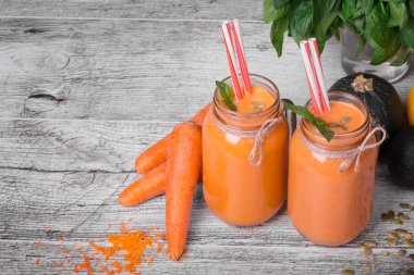 Gri bir arka plan büyük mason kavanoz olgun kesilmiş havuç ve yeşil bitki ile iki Portakallı gazoz kadeh en iyi bir görünüm.