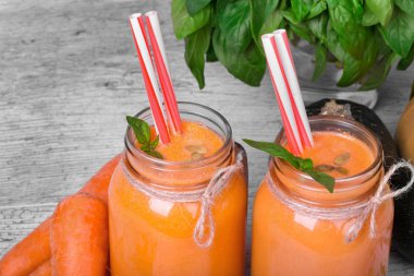 İki portakal meşrubat mason kavanoz içinde bir görünüm yukarıdan. Detoks smoothies olgun kesilmiş havuç ve yeşil bitki üzerinde gri bir arka plan ile.