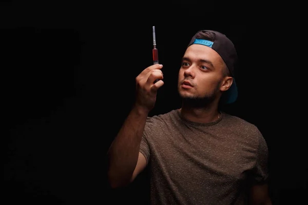 Mladý drogový závislý chlapík s injekční stříkačkou, zařízení pro vstřikování drogy na černém pozadí.. — Stock fotografie