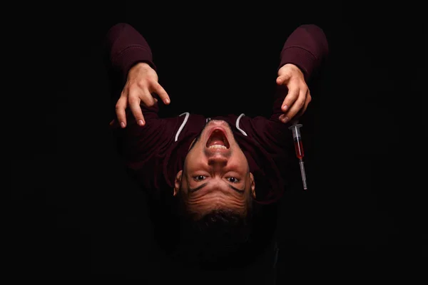 A drug addict junkie in a purple sweat-shirt suffers from a drug addiction on a dark black background. — Stock Photo, Image