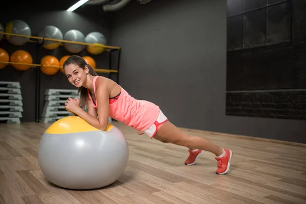 Hübsches, lächelndes Mädchen mit einem Fitnessball. Frauen, die auf einem verschwommenen Hintergrund im Fitnessstudio trainieren. Aerobic-Konzept. Kopierraum. — Stockfoto