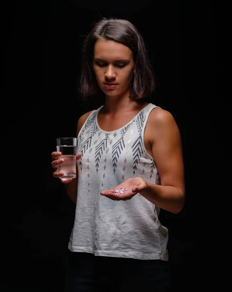 Une femme qui prend des médicaments. Fille de sport moderne regardant les vitamines dans les comprimés sur un fond noir. Concept de contraception . — Photo