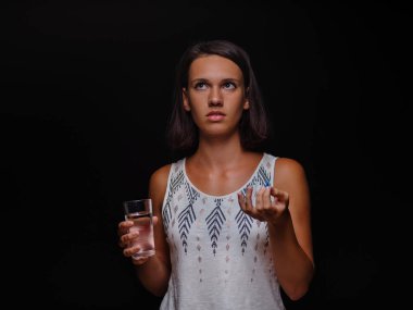 Siyah bir arka plan üzerine bir bardak su ve alma hapları tutan genç kadın. Tıbbi yardım, tıp kavramı. Kopya alanı.