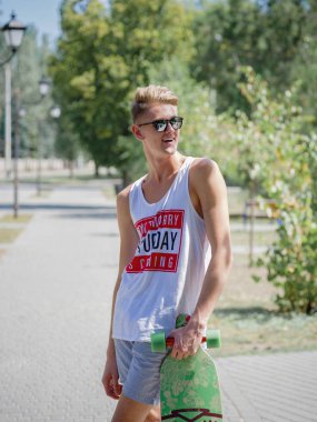 Bir kaykay üzerinde doğal renkli bir arka plan ile yakışıklı bir genç adam. Bir güneş şık bir adam açık havada içinde gözlük.