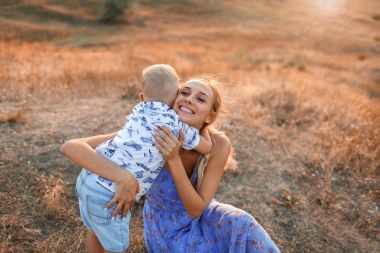 Çok güzel bir küçük oğlu doğa arka plan üzerinde çekici genç kadın var. Bir çocuk annesi bir sahada sarılma.