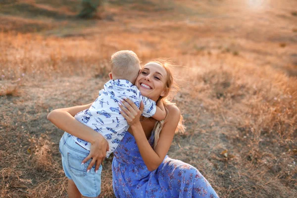 Çok güzel bir küçük oğlu doğa arka plan üzerinde çekici genç kadın var. Bir çocuk annesi bir sahada sarılma.