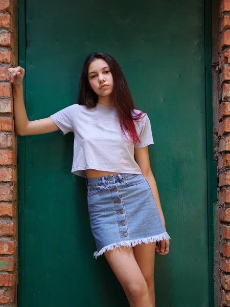 Um retrato de uma menina bonita com cabelo escuro em roupas casuais posando em um fundo de porta verde. Conceito urbano moderno . — Fotografia de Stock