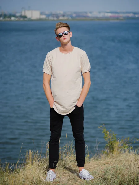 Joven con estilo en gafas de sol. Alto, chico guay caminando cerca del río sobre un fondo borroso. Concepto de estilo universitario . —  Fotos de Stock