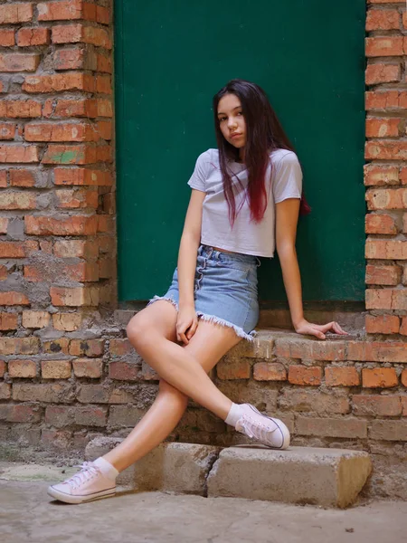 Bir portre rahat kıyafetler bir yeşil kapı arka plan üzerinde poz koyu saçlı güzel bir kız. Modaya uygun kentsel kavramı.