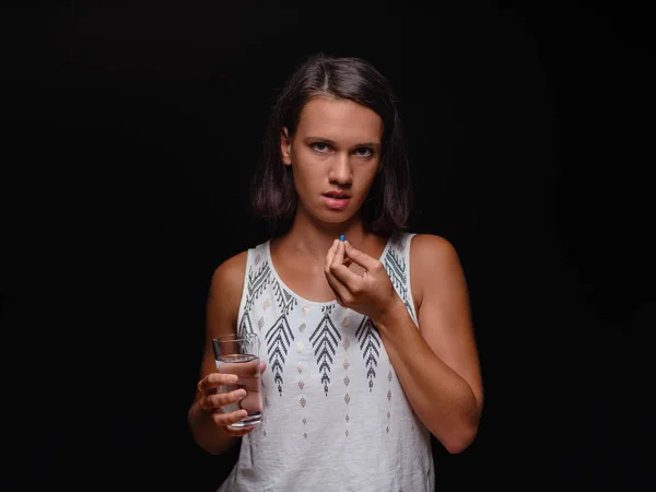 Ung kvinna med ett glas vatten och ta piller på en svart bakgrund. Läkarvård, medicin koncept. Kopiera utrymme. — Stockfoto