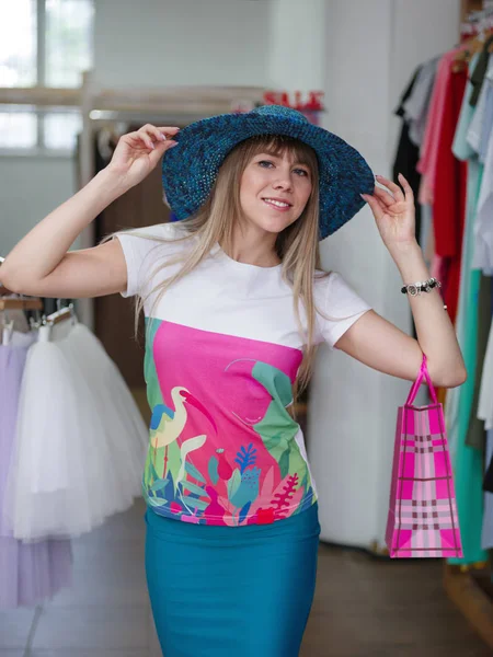 Uma senhora atraente em um chapéu de javali azul faz compras em um fundo de loja de roupas. Conceito de venda e moda . — Fotografia de Stock