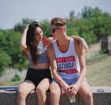 Doğal bir arka plan üzerinde oturan iki pozitif, serin gençler. Sevimli Romantik Çift bir şehir parkı. Romantik tatil kavramı.