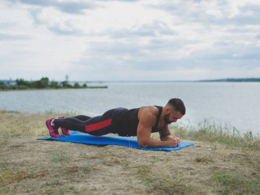 Güçlü bir vücut geliştirmeci bir tahta üzerinde doğal arka plan bulanık bir nehir kıyısında ayakta dövme.