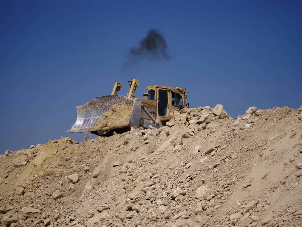 Een backhoe loader, loader backhoe, digger op een hoop zand en stenen op een natuurlijke achtergrond. — Stockfoto