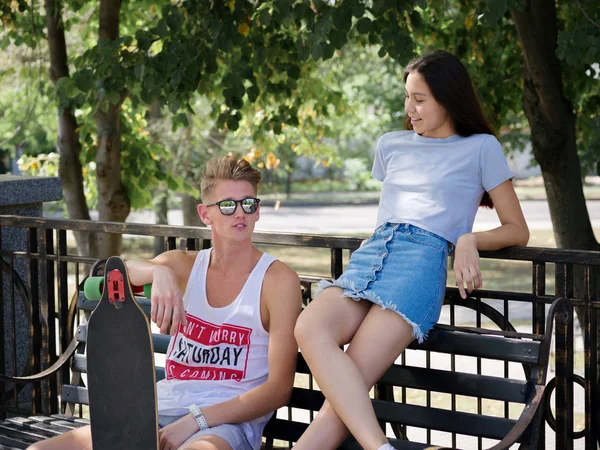 Un couple d'adolescents sortir ensemble dans un parc, une belle fille et un camarade assis sur un banc sur un fond naturel flou . — Photo