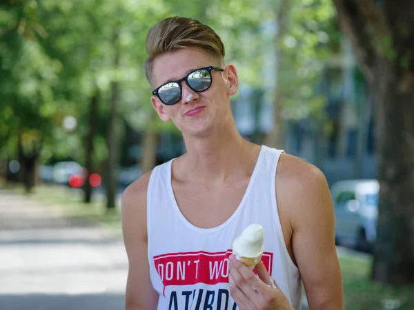 Un tipo atractivo en gafas de sol comiendo un helado en un parque sobre un fondo borroso natural . —  Fotos de Stock