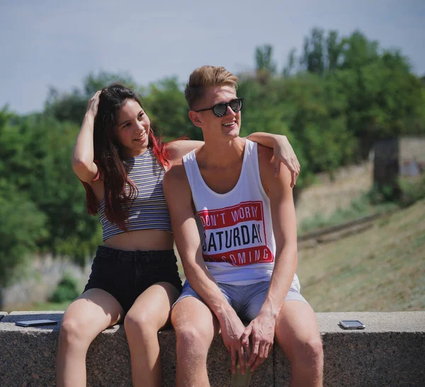 Doğal bir arka plan üzerinde oturan iki pozitif, serin gençler. Sevimli Romantik Çift bir şehir parkı. Romantik tatil kavramı.