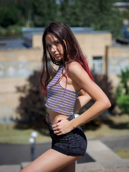 Uma menina hipster atraente em roupas casuais sentado em um fundo urbano. Moda, conceito de juventude . — Fotografia de Stock