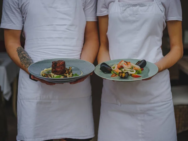 Un par de camareros sosteniendo platos. Camarero y camarera sirviendo comida sobre un fondo borroso. Concepto de restaurante clásico . — Foto de Stock