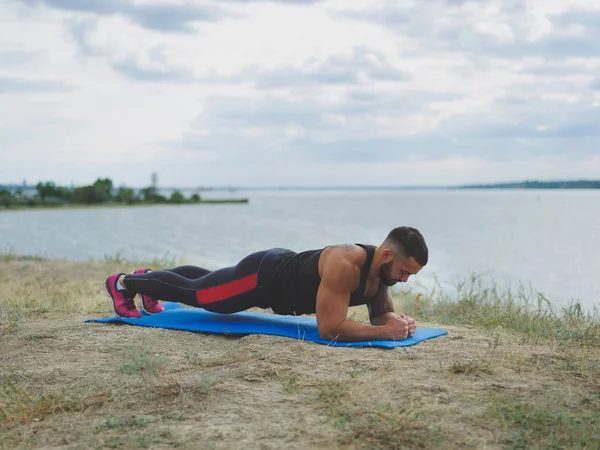 Güçlü bir vücut geliştirmeci bir tahta üzerinde doğal arka plan bulanık bir nehir kıyısında ayakta dövme.