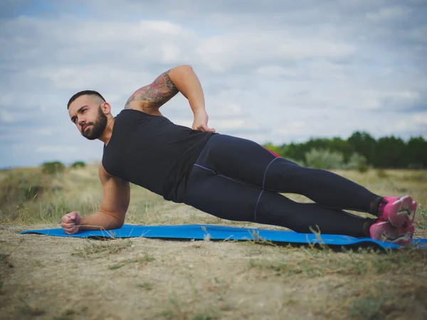 Güçlü bir vücut geliştirmeci bir tarafı tahta üzerinde doğal arka plan bulanık bir nehir kıyısında ayakta dövme.