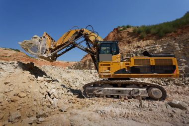 Mavi gökyüzü ve kumlu taş ocağı arka plan üzerinde yeni bir inşaat sitesinde büyük bir sarı Ekskavatör bir close-up.