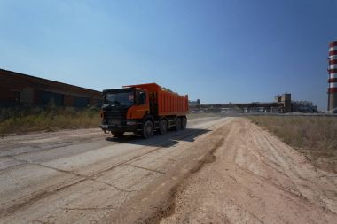 Bir büyük Turuncu İpucu kamyon doğal bir arka plan üzerinde bir yolda sürüş bir gölge ile. Bir kum ocağında büyük taşıyıcı.