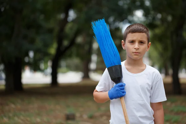 Ett litet barn i en vit T-shirt stående med en blå kvasten på en suddig naturliga bakgrund. Ekologi, föroreningar koncept. — Stockfoto