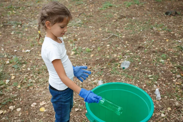 Childs kezét a kék latex kesztyű színes újra feldolgoz. Külső fénykép, a föld és a szemetet a háttérben. — Stock Fotó