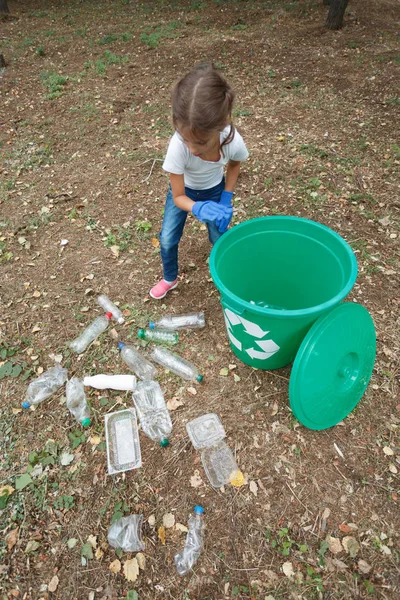 Barn i blå latex handskar, kasta plastpåsen i återvinning bin. Mark och skräp på bakgrunden. — Stockfoto