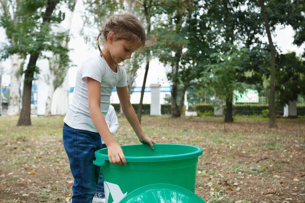 En söt liten flicka som innehar en stor grön återvinning bin på en suddig naturliga bakgrund. Ekologi föroreningar koncept. — Stockfoto