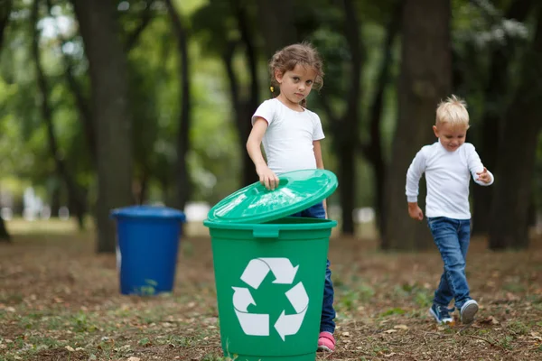 Una niña poniendo una tapa de cubo en una papelera de reciclaje verde sobre un fondo natural borroso. Ecología y niños . — Foto de Stock