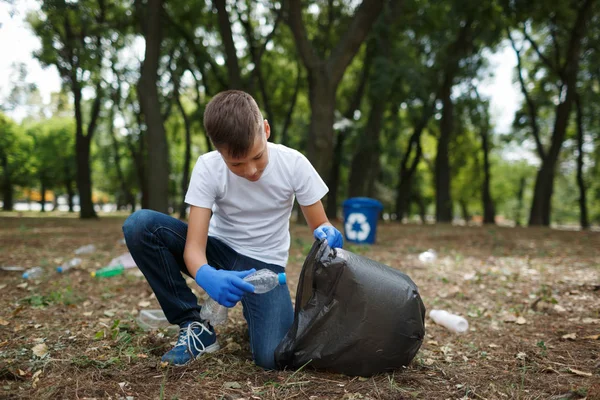 Ett litet barn plocka upp skräp och sätta den i en svart sopsäck på en naturlig bakgrund. Ekologi skydd koncept. — Stockfoto