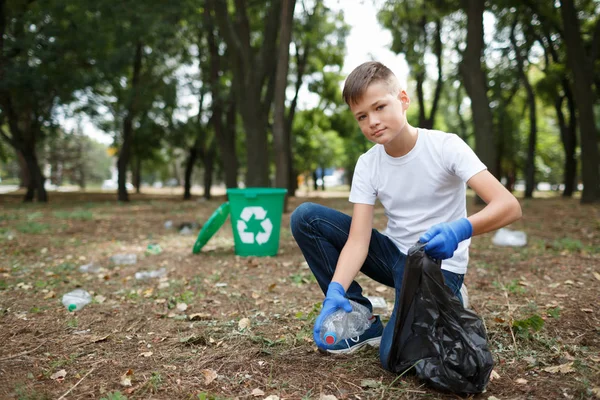 小さな子供のゴミ拾いと自然な背景に黒いゴミ袋にそれを置きます。生態保護概念. — ストック写真