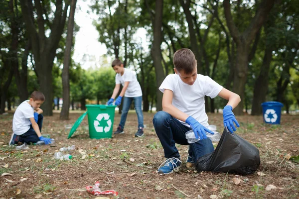 Un niño pequeño recogiendo la basura y poniéndola en una bolsa de basura negra sobre un fondo natural. Concepto de protección ecológica . — Foto de Stock