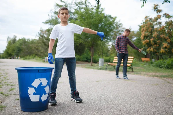 En allvarlig pojke visar en dålig kille tumme ner. En ung man som kastar bort en plastflaska i mitten av vägen. — Stockfoto