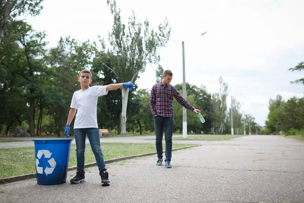 En allvarlig pojke visar en dålig kille tumme ner. En ung man som kastar bort en plastflaska i mitten av vägen. — Stockfoto