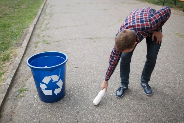 緑のごみ箱にそれを投げるためにプラスチック製のボトルを拾う若い男。良き市民は気の性質. — ストック写真