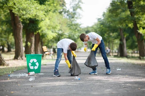 黒いゴミ袋を押しながら公園の背景にプラスチック製のごみを収集の男の子のカップル。生態保護概念. — ストック写真