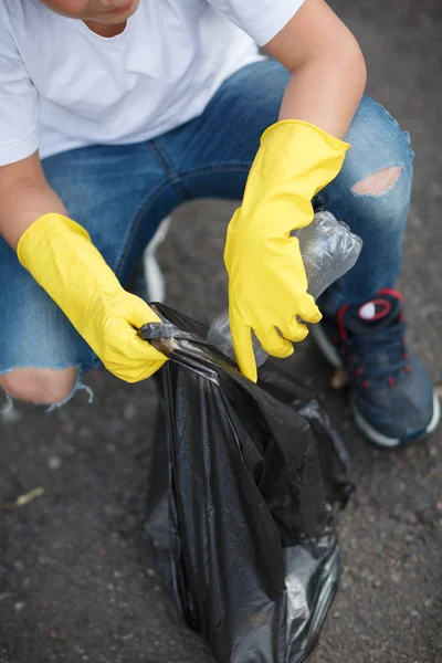 Childs händer i gul latex handskar håller en svart sopsäck på en asfalt bakgrund. Ekologi skydd koncept. — Stockfoto