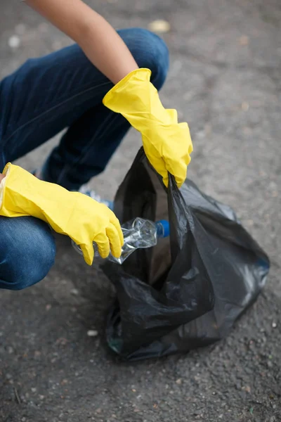 チャイルズはアスファルトの背景に黒いゴミ袋を保持している黄色のラテックス手袋の手します。生態保護概念. — ストック写真