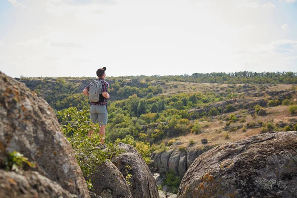 Fiatalember backpack nézek a távolba hegyek tetején. Egy turista a természetes háttér. — Stock Fotó