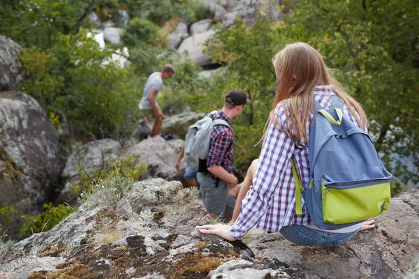 Drie jonge mensen klimmen van de rotsachtige heuvel. Een bedrijf van vrolijke reizigers op een onscherpe achtergrond van de natuurlijke. — Stockfoto