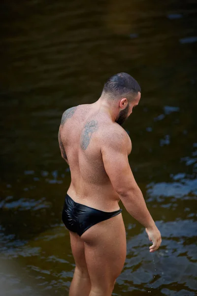 Μια μυϊκή σέξι άνδρας στο κολυμβητικό ψάχνει στο βάθος στην ακτή της θάλασσας. Ένας κολυμβητής σε φόντο νερού. — Φωτογραφία Αρχείου