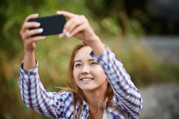 Beautiful young woman taking picture of herself. Selfie on a blurred natural background. Filtered image. — Stock Photo, Image