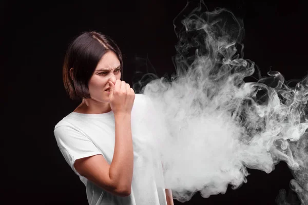 Жінка зморщується через сигарету або електронний дим на темно-сірому тлі. Концепція охорони . — стокове фото