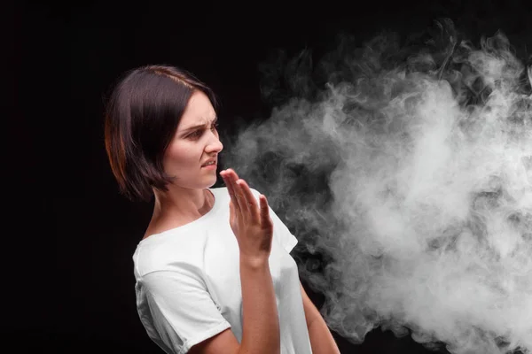 Mladá žena nemá rád kouř z cigarety nebo elektronická cigareta na černém pozadí. Koncepce zdraví. — Stock fotografie