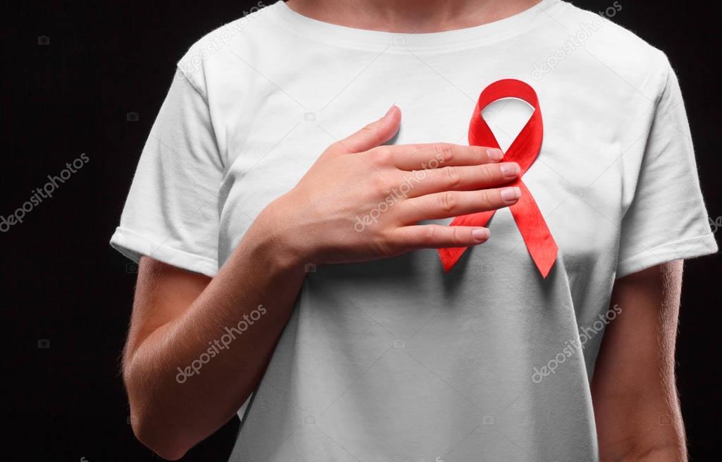 A female with a red ribbon on a white T-shirt on a black background. Modern treatment and healthcare. AIDS awareness concept.